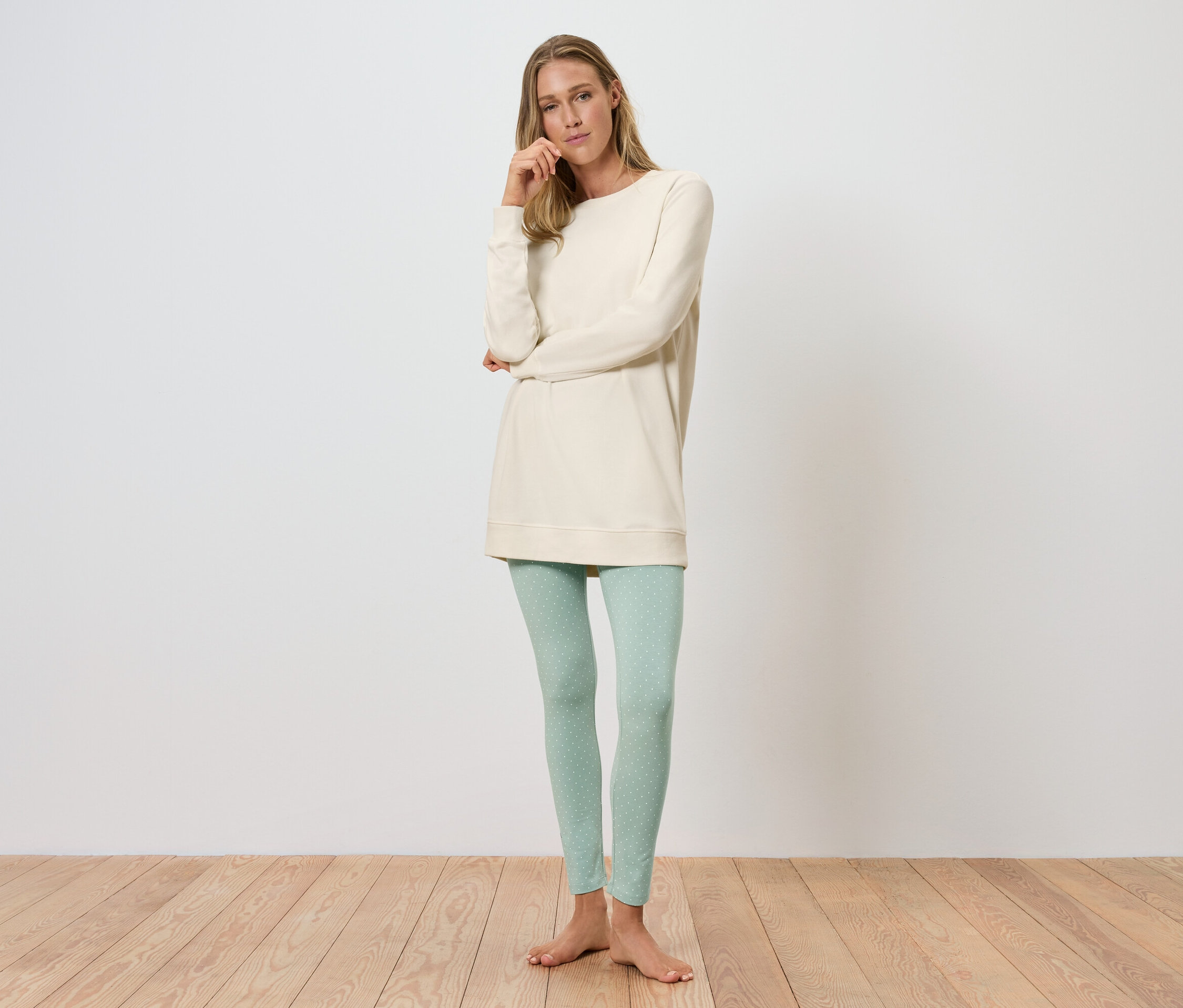 Eine Frau steht und posiert in einer cremefarbenen Tunika und hellgrünen Leggings.