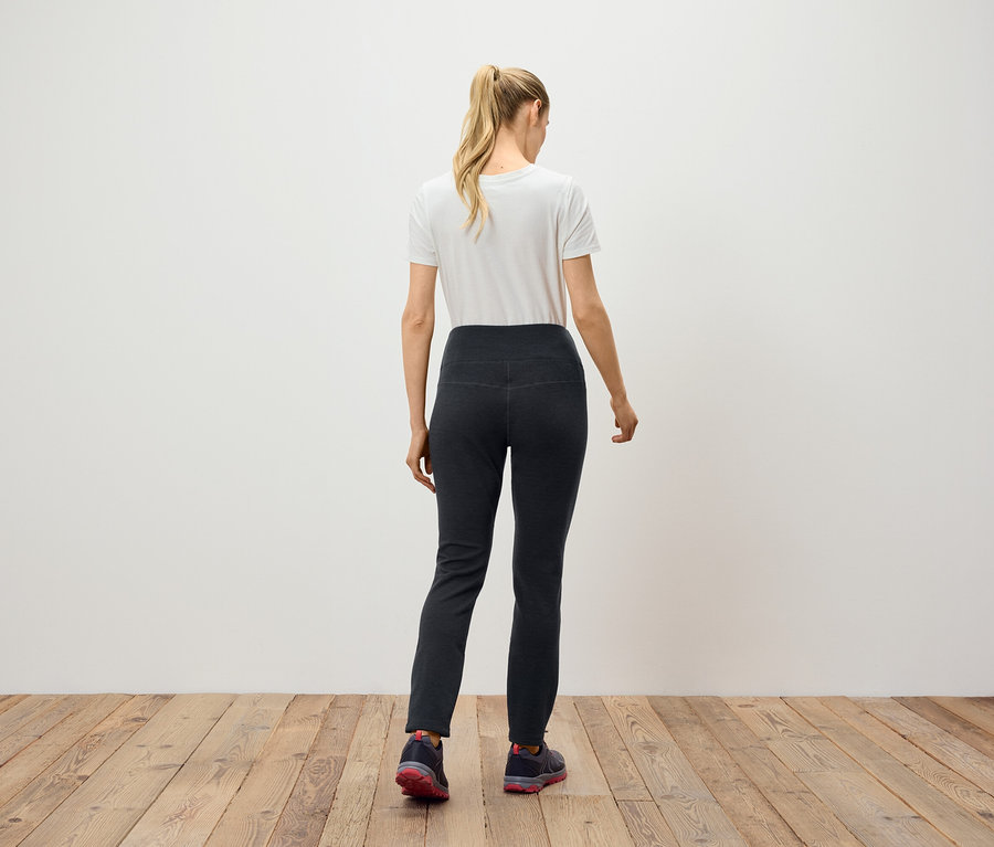 Frau mit blonden, zum Pferdeschwanz gebundenen Haaren steht mit dem Rücken zur Kamera und trägt eine schwarze Hose und ein weißes T-Shirt.