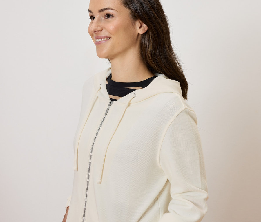 Frau posiert in cremefarbener Reißverschluss-Jacke.
