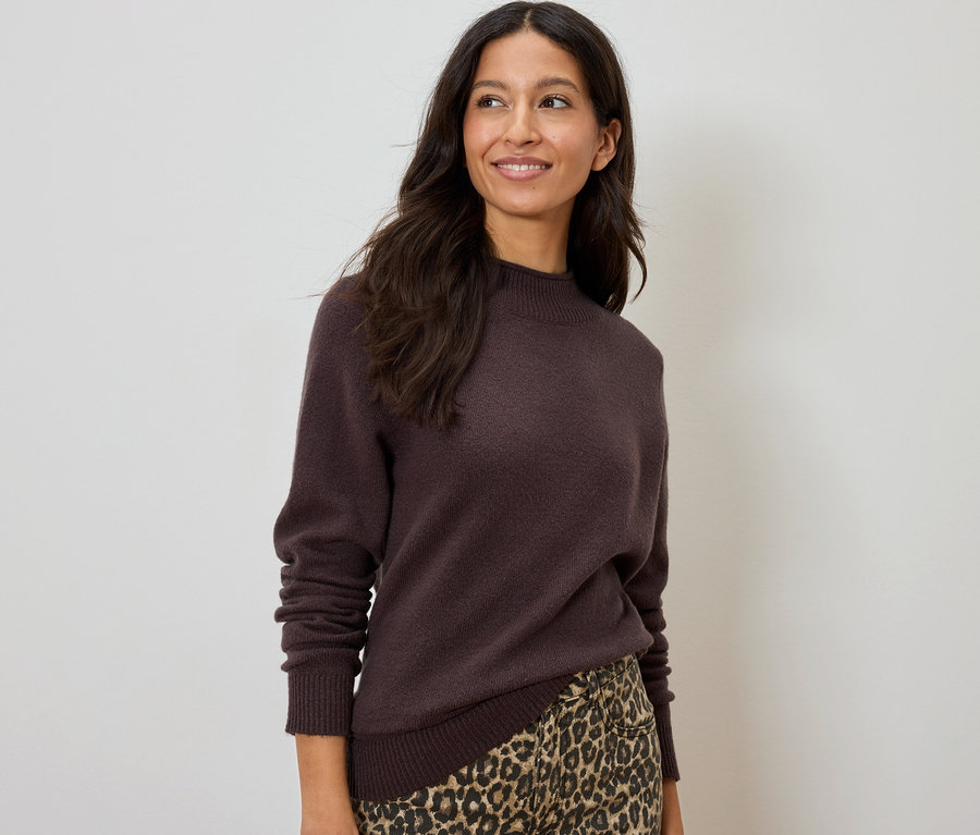 Frau lächelt und trägt einen braunen Pullover und einen Rock mit Leopardenmuster.