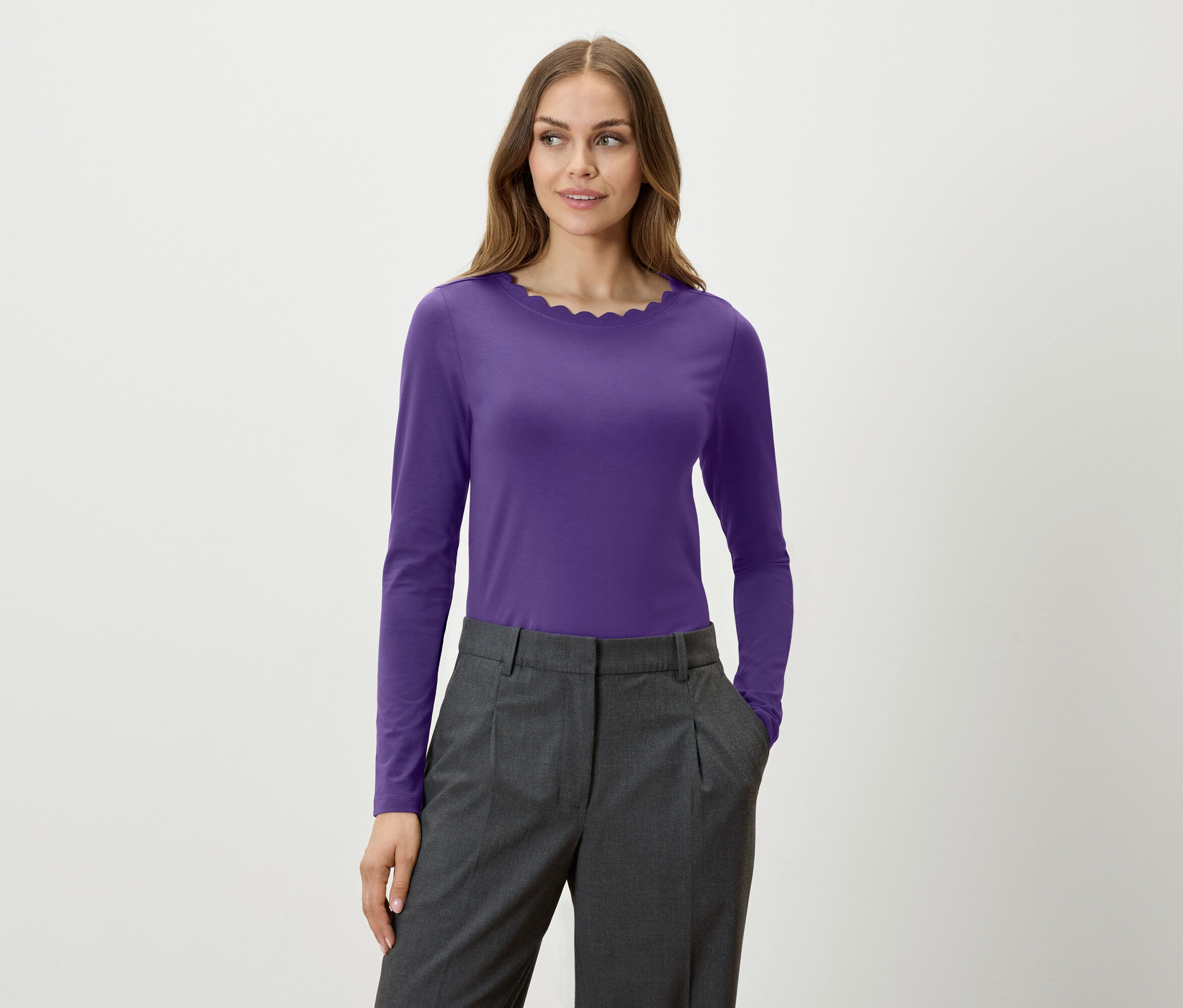 Eine Frau trägt ein violettes Langarmshirt und eine graue Hose.