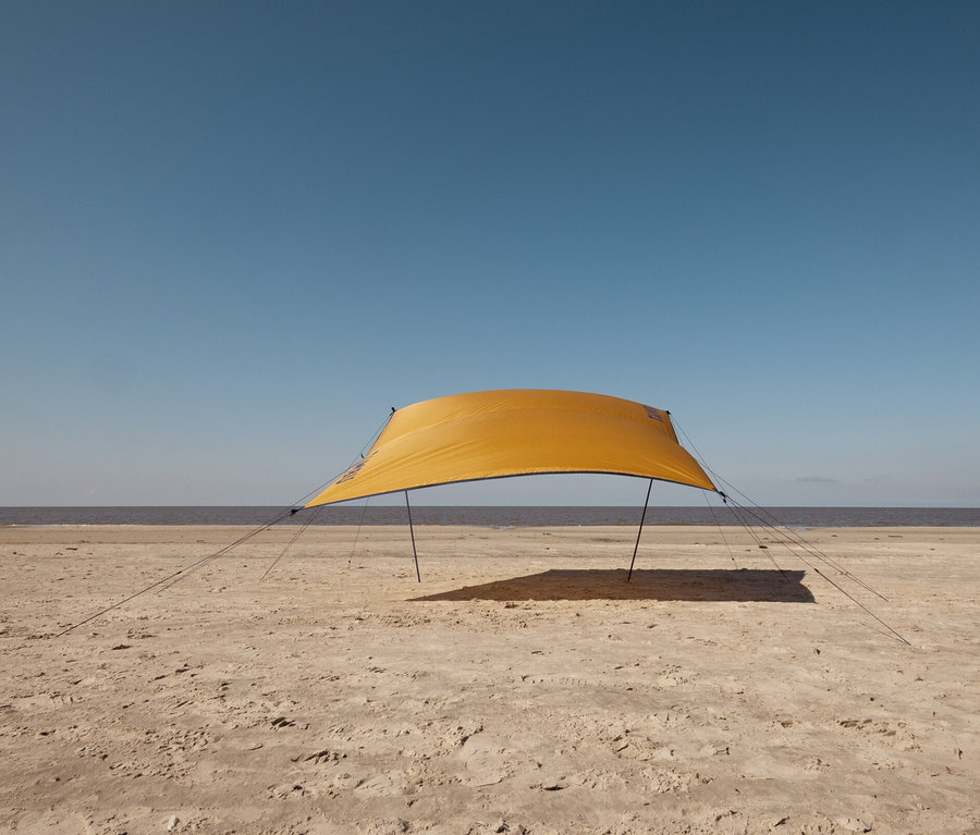 Ein kleines, gelbes Tambu Sonnensegel CHADA steht am Sandstrand in der Nähe des Meeres.