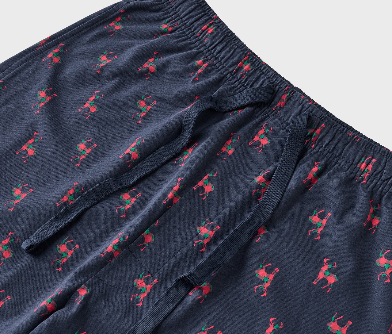 Detail einer blauen Pyjamahose mit roten Rentieren und grünen Sätteln.