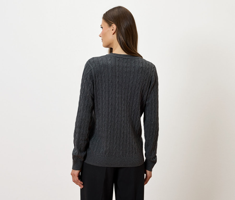 Frau steht mit dem Rücken zur Kamera und trägt einen grauen Strickpullover und eine schwarze Hose.