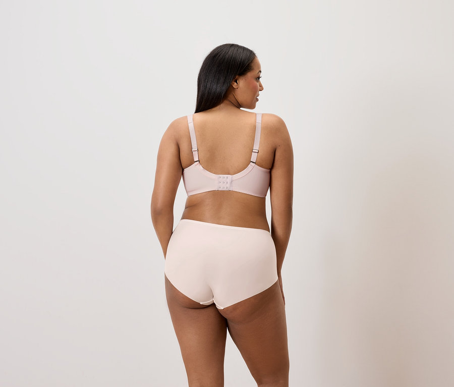 Rückansicht: Frau mit dunklem Haar trägt einen hellrosa BH und Höschen.