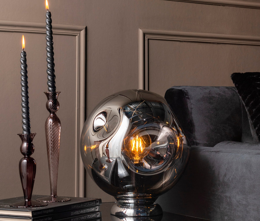 Schwarze Kerzen in braunen Kerzenständern und eine Glaslampe auf einem Tisch.