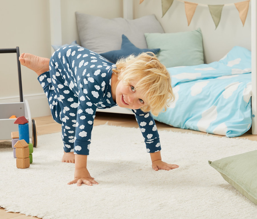 Kind im blauen 3er-Set Schlafanzug aus Bio-Baumwolle macht einen Handstand neben dem Bett.