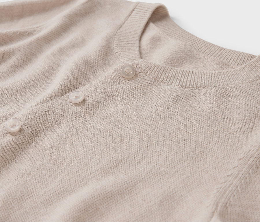 Detailansicht einer beigen Strickjacke mit Rundhalsausschnitt und Knöpfen.