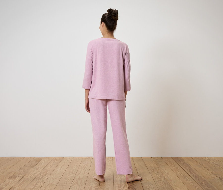 Eine Frau steht mit dem Rücken zur Kamera und trägt einen rosa Pyjama.