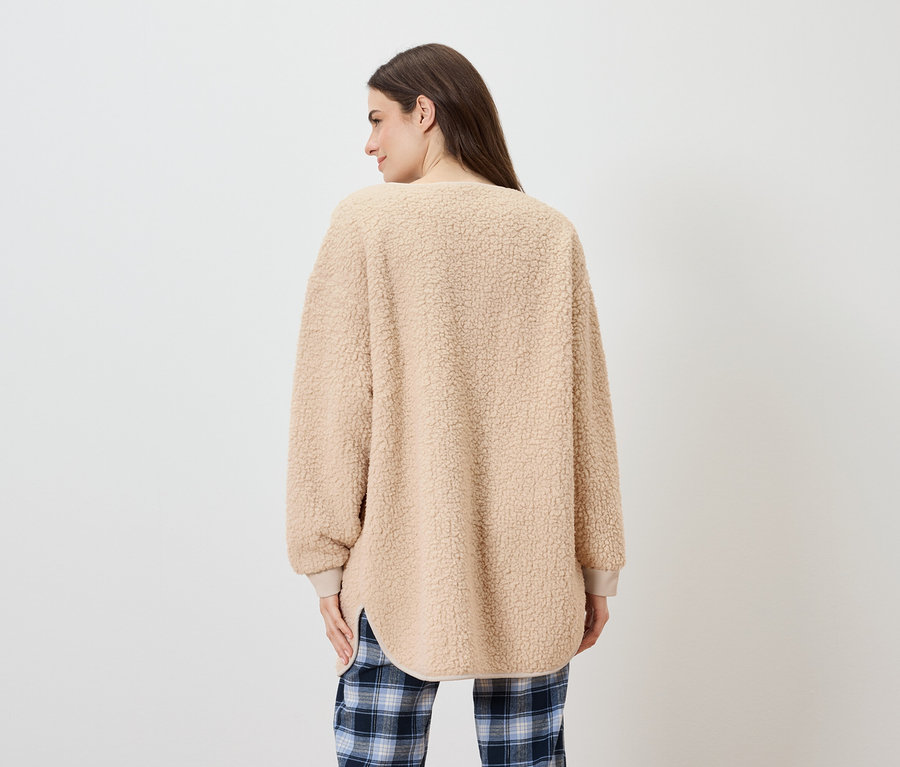 Frau mit dem Rücken zur Kamera trägt einen beigen, zotteligen Pullover und eine blau karierte Hose.