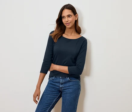 Frau posiert in marineblauem Dreiviertelarm-Shirt und blauen Jeans.