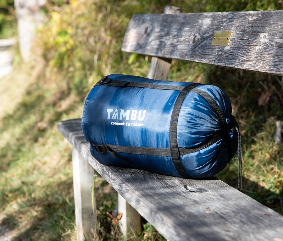 Ein blau verpackter Tambu Talu 1500 Mumienschlafsack liegt auf einer Holzbank.