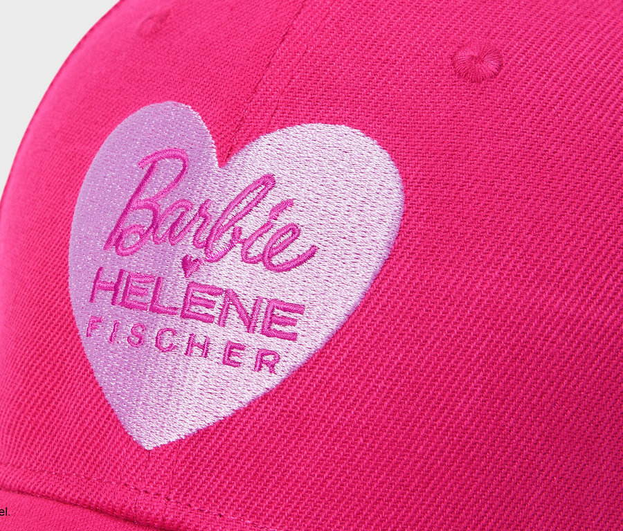 Nahaufnahme einer pinkfarbenen Kappe mit aufgesticktem, hellrosa Herz, das den Schriftzug "Barbie HELENE FISCHER" enthält.