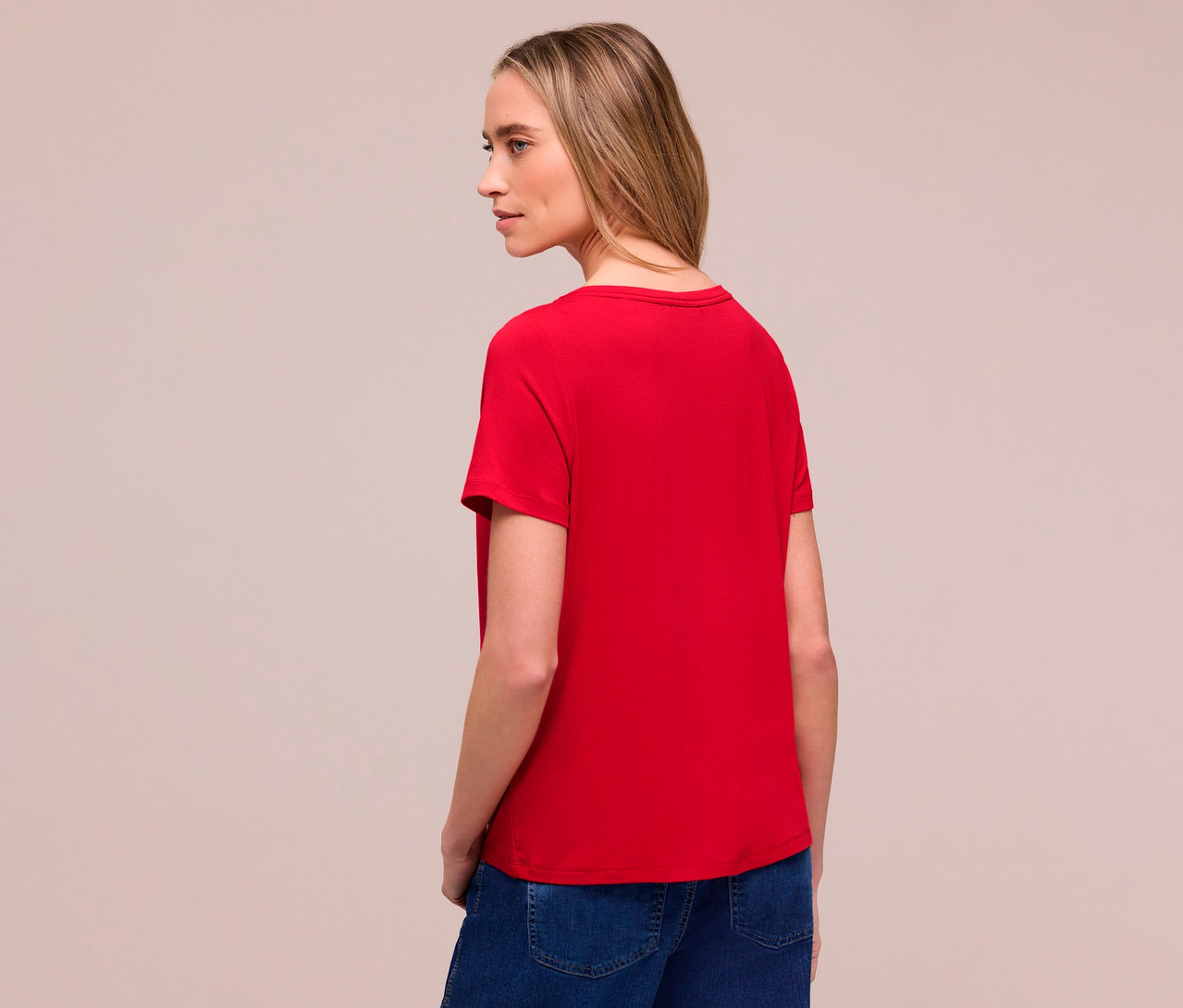Frau von hinten mit rotem Street One T-Shirt und Jeans. Sie blickt nach links.