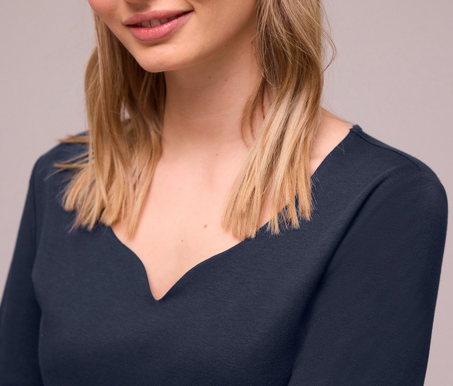 Lächelnde junge Frau mit blonden Haaren trägt ein navyblaues Street One Kurzarmshirt mit geschwungenem V-Ausschnitt.