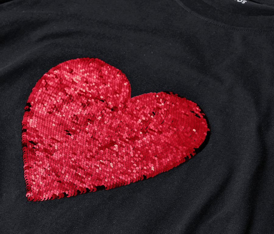 Auf einem schwarzen T-Shirt ist ein großes, rotes Herz aus Pailletten abgebildet.