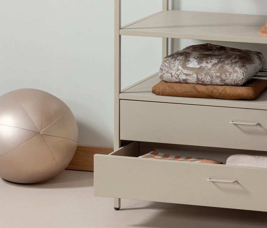 Ein WOOOD offener Metall-Kleiderschrank »Ferris«, 100 cm steht neben einem beige Gymnastikball. Die untere Schublade des Schranks ist geöffnet.