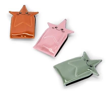 Drei glänzende, sternförmige Etuis in Orange, Rosa und Salbeigrün, jedes mit einem lächelnden Cartoon-Gesicht, diagonal auf weißem Hintergrund angeordnet.