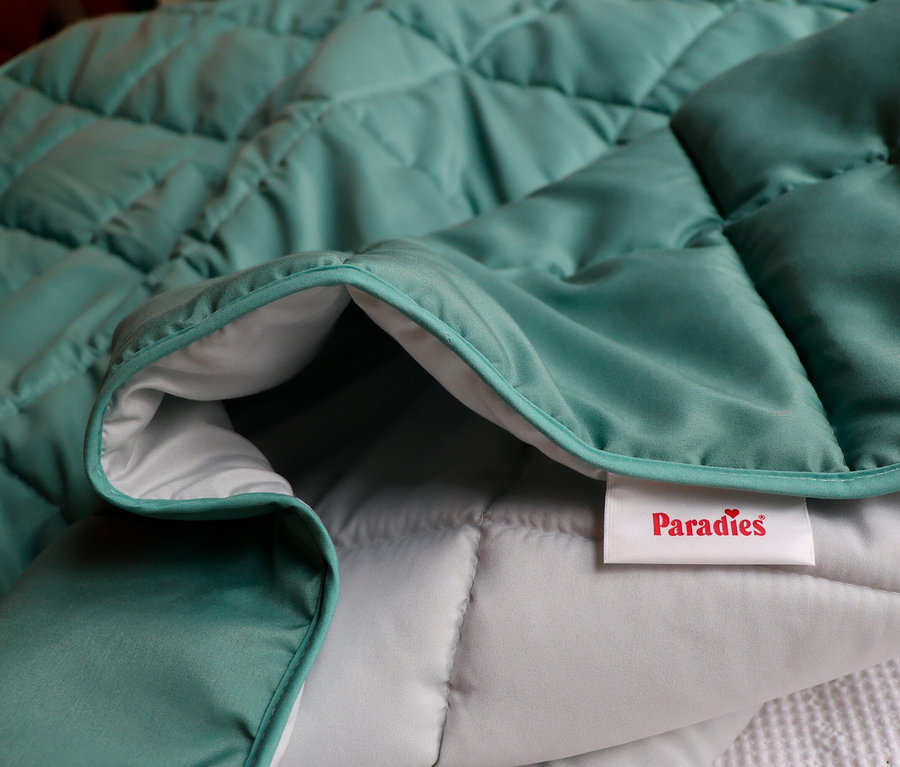 Nahaufnahme einer gesteppten, türkisfarbenen Decke mit grauer Innenseite und einem weißen Etikett mit der Aufschrift "Paradies".