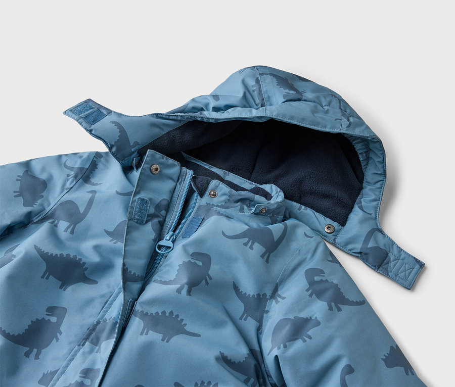 Nahaufnahme einer blauen Jacke mit Kapuze und Dinosaurier-Muster, die teilweise geöffnet ist und ein marineblaues Fleecefutter zeigt.
