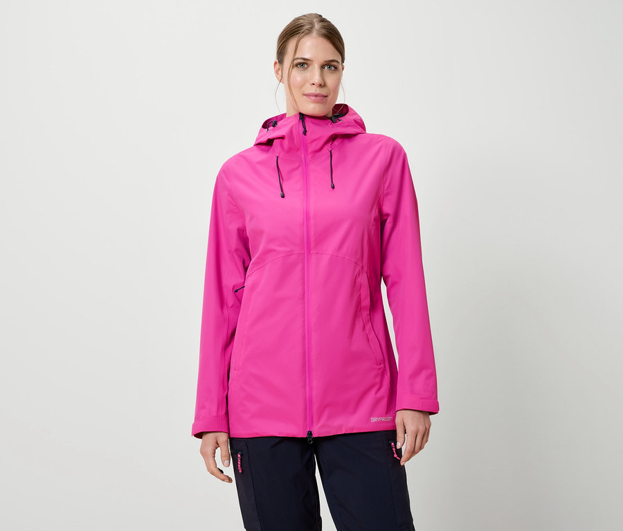 Frau trägt eine pinke Regenjacke mit Kapuze und dunkelblaue Hosen vor einem weißen Hintergrund.