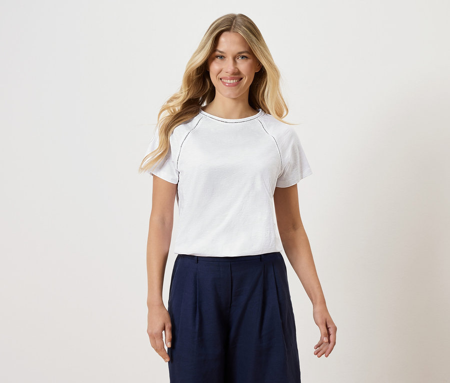 Frau trägt ein weißes T-Shirt mit marineblauen Culottes vor einem weißen Hintergrund.
