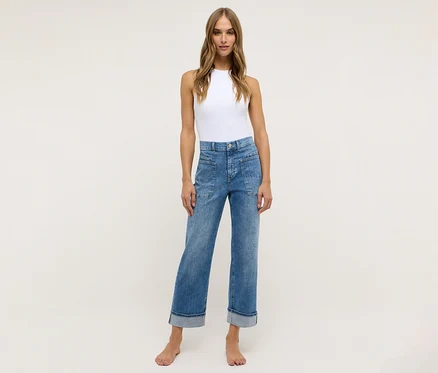 Eine Frau steht barfuß da und trägt einen weißen Body und blaue Angels Denim »Liberta« Jeans.