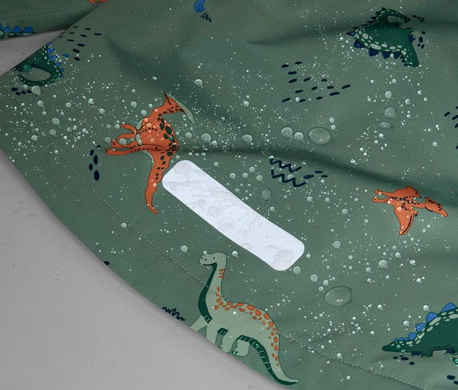 Nahaufnahme eines grünen Stoffes mit Dinosaurier-Muster und Wassertropfen, sowie einem reflektierenden, rechteckigen Aufnäher.