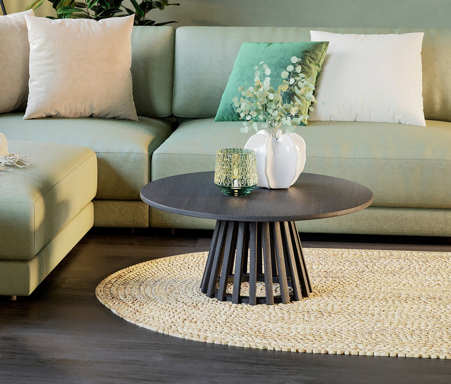 Runder, dunkler Holztisch mit Dekorationen auf einem beige Teppich vor einem hellgrünen Sofa.