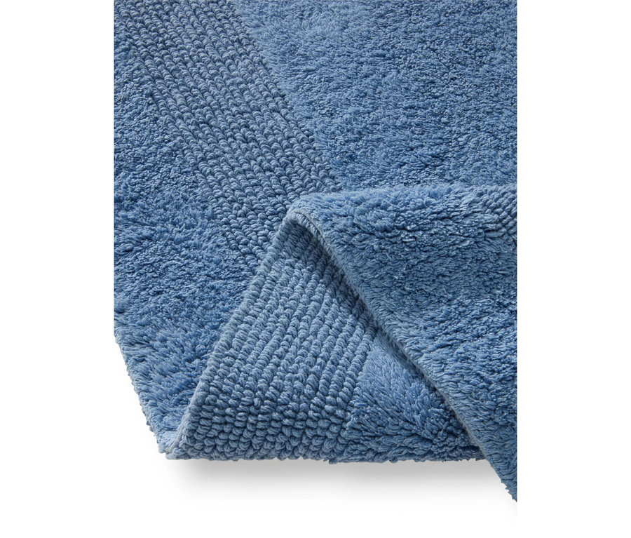Nahaufnahme einer blauen Badematte, gefaltet, um ihre plüschige und gerippte Textur zu zeigen.