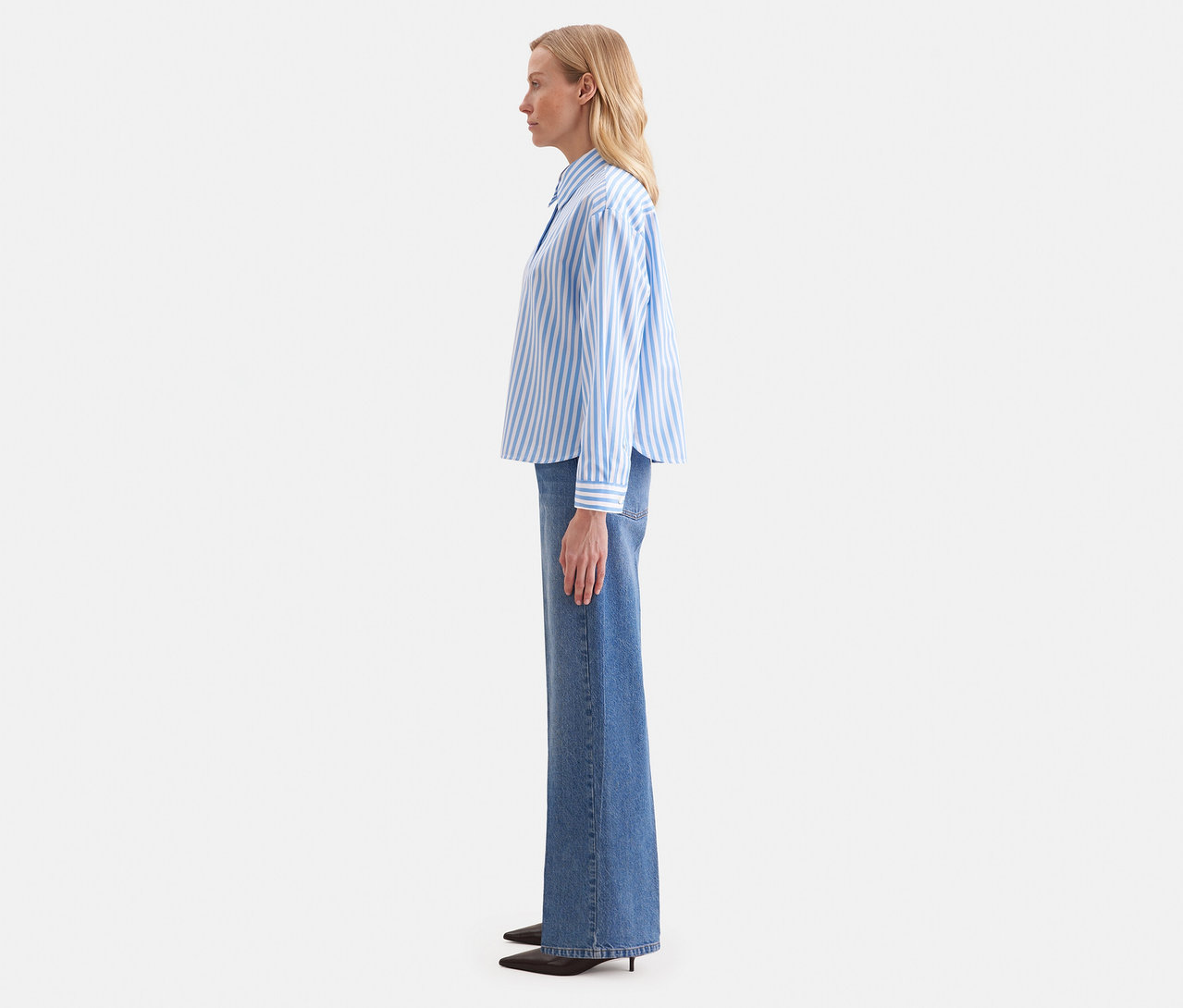 Frau im Profil trägt eine blau-weiß gestreifte Seidensticker Oversize Hemdbluse und weite Jeans.