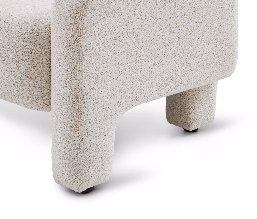 Unterer Teil eines cremefarbenen, strukturierten Sessels oder Sofas, der zwei kurze, dicke Beine mit schwarzen Gleitern auf weißem Hintergrund zeigt.