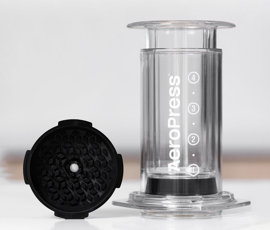 Durchsichtiger AeroPress Coffee Maker »Clear« steht neben einem schwarzen Zubehörteil.