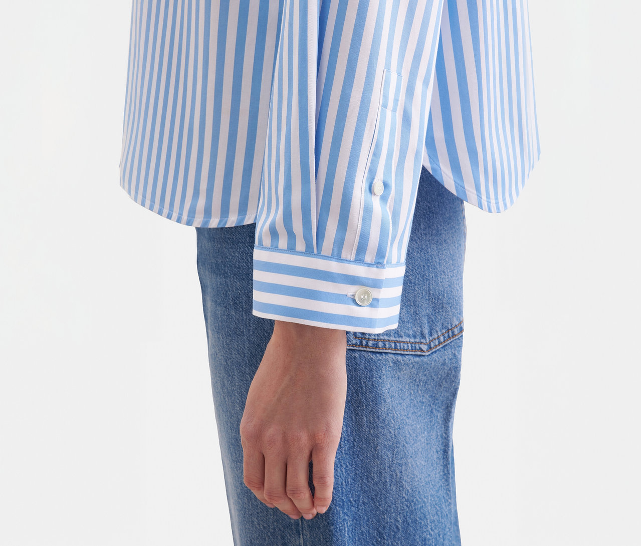 Nahaufnahme einer Person in einer blau-weiß gestreiften Seidensticker Oversize Hemdbluse mit geknöpften Manschetten, kombiniert mit blauen Jeans.