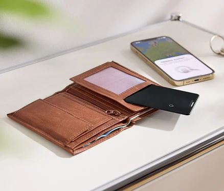 Braunes, offenes Portemonnaie, schwarze Karte, goldenes Mobiltelefon und Schlüssel auf einer weißen Oberfläche.