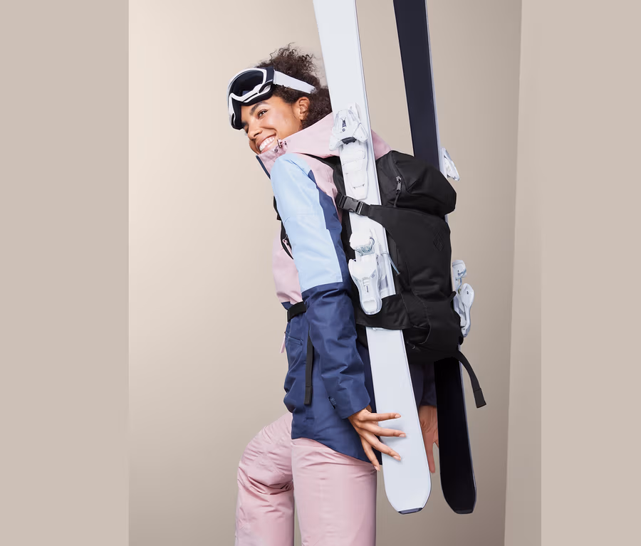 Frau lächelt und trägt Ski mit Ski-Rucksack.