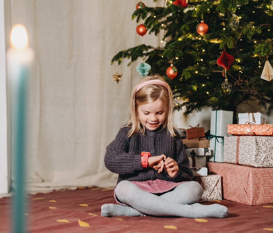 Ein Mädchen sitzt vor einem Weihnachtsbaum und betrachtet ihre pinke Kids Watch Xplora XGO3 2nd Gen.