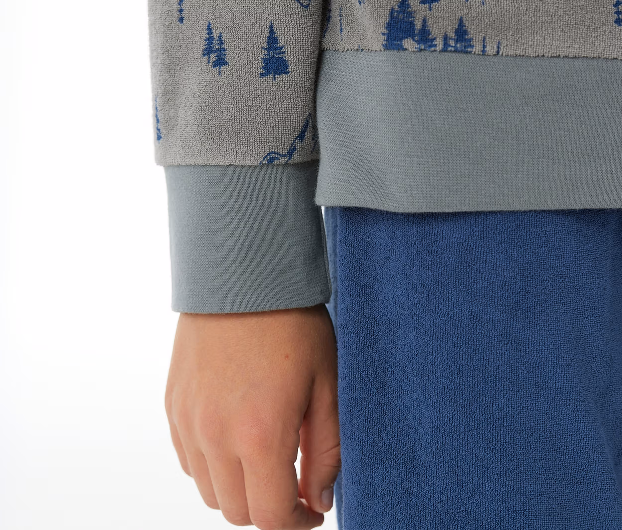 Kind trägt SCHIESSER Kinder-Pyjama mit Bündchen: graues Oberteil mit blauen Baummotiven und blaue Hose.