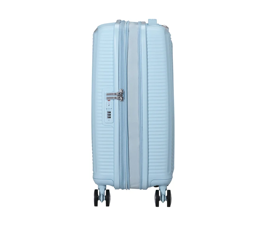 Ein kleiner, pastellblauer American Tourister Hartschalen-Koffer »Soundbox« Spinner steht aufrecht, mit gerippter Textur, zentralem Reißverschluss, silbernem Zahlenschloss und vier schwarzen Rollen.