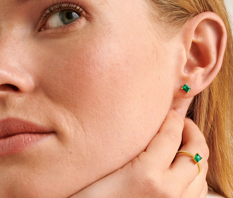 Detailaufnahme vom Gesicht einer blonden Frau mit einem 585 Gold Ring und Ohrsteckern mit grünem Zirkonia.