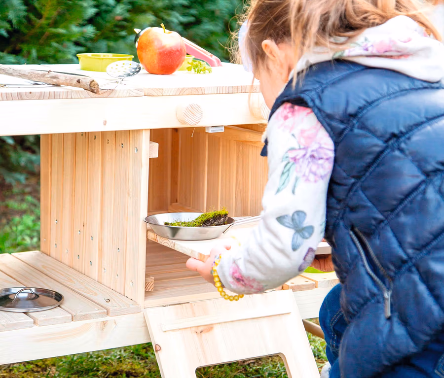 Mädchen spielt mit small foot Matschküche Spielzeug draußen auf dem Rasen.