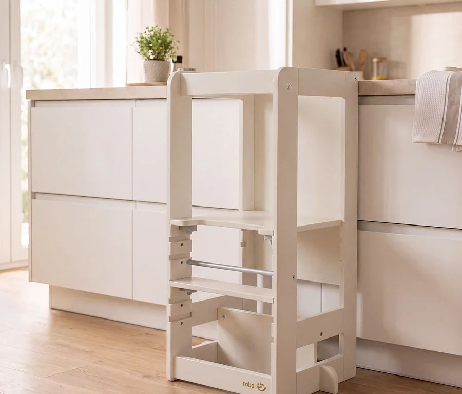 Heller, beigefarbener Lernturm aus Holz mit verstellbarer Plattform und Sicherheitsbügel, neben einer modernen Küchenzeile mit hellen Schränken und einer Pflanze.
