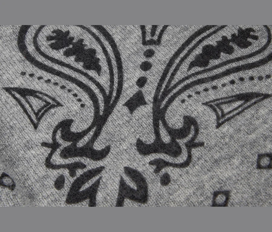 Nahaufnahme eines grauen Strick-Bandanas mit Wolle und Kaschmir, das ein dunkelgraues Paisley-Muster zeigt.