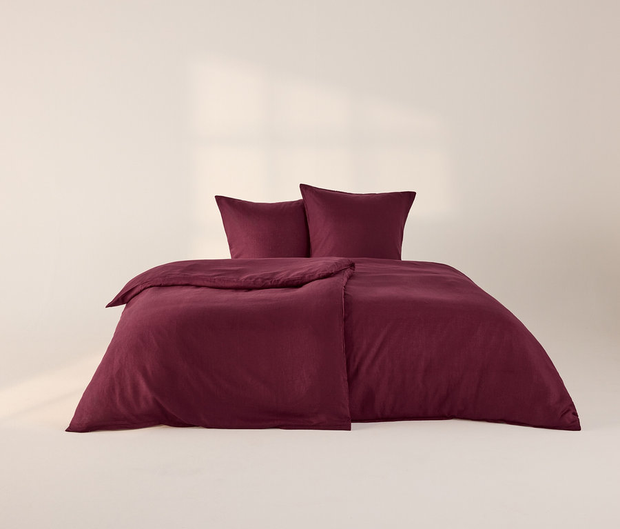 Beerenfarbene Leinen-Bettwäsche auf einem Bett, bestehend aus einem Bettbezug und zwei Kissenbezügen. Der Bettbezug ist leicht gefaltet, die Kissen liegen am Kopfende.