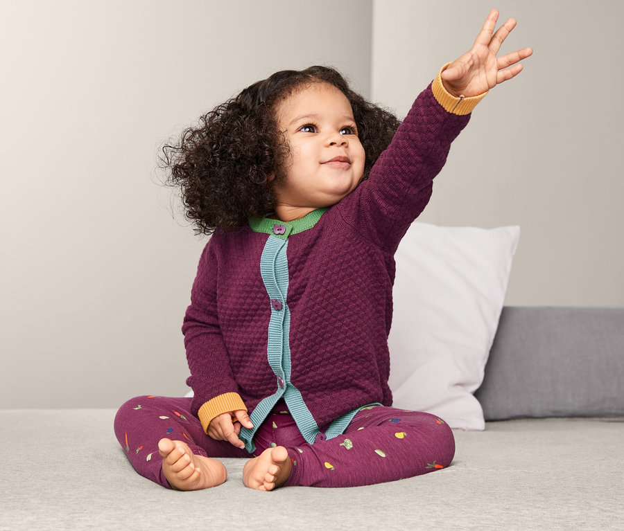 Mädchen sitzt mit erhobenem Arm und trägt eine Strickjacke.
