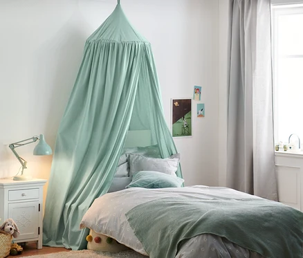 Grüner Betthimmel über Bett im Kinderzimmer. Auf dem Nachttisch steht eine Lampe, im Korb Kuscheltiere.