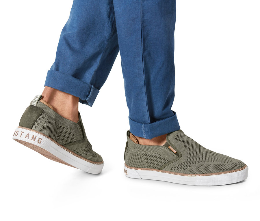 Eine Person trägt einen khaki Slipper »Mustang«. Der Slipper hat eine weiße Sohle.
