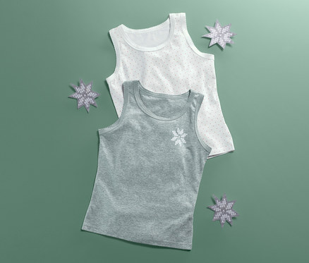 Zwei Unterhemden liegen auf einem grünen Hintergrund, eines grau und eines weiß gepunktet, beide mit Schneeflocken und Deko.