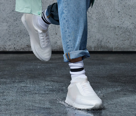Bein in Jeans und Regen-Überziehschuhen tritt in eine Pfütze.
