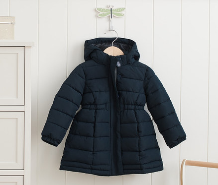 Eine dunkelblaue Thermoparka hängt an einer weißen Wand neben einer Kommode mit Wolkenknöpfen.